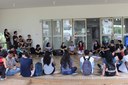 Jovens sentados no chão, formando uma roda, conversam em frente à entrada de laboratórios da UNILA