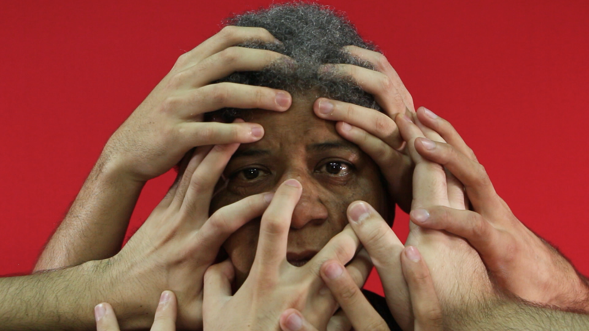 fotografia de uma mulher negra olhando para a frente e com várias mãos brancas sobre seu rosto