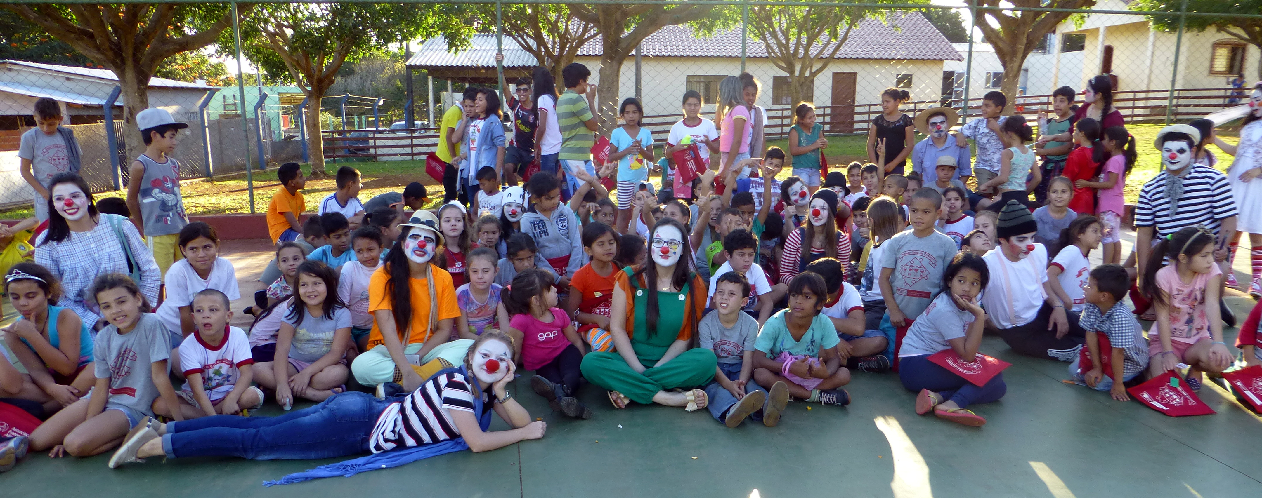 Foto de estudantes que integram o grupo Eternizar-te, vestidos de palhaço, com crianças
